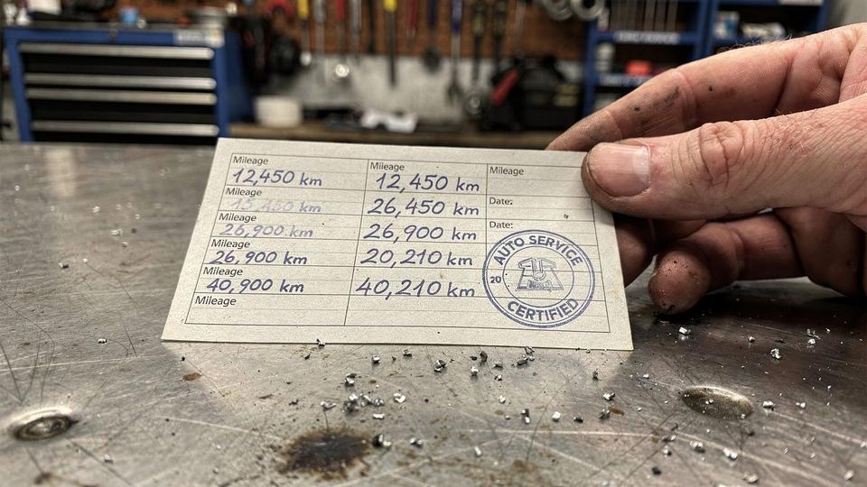 Printed service record card with handwritten mileage entries and an ink stamp on a workshop desk